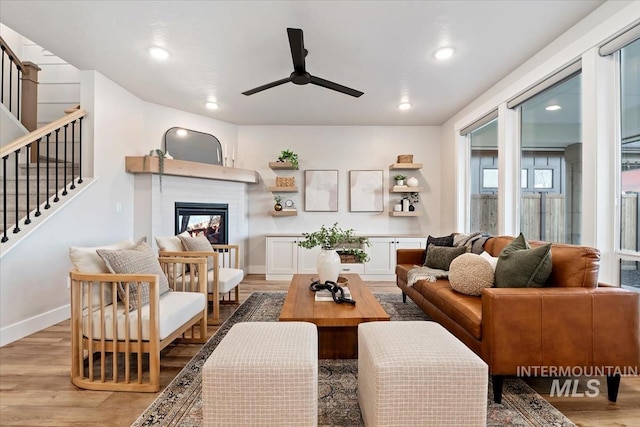 living room with stairway, light wood-style floors, a ceiling fan, a multi sided fireplace, and baseboards