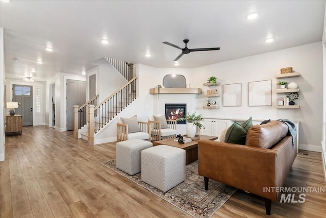 living room with baseboards, a ceiling fan, a glass covered fireplace, stairs, and light wood-type flooring