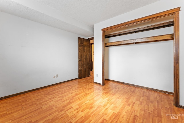 unfurnished bedroom with a closet, a textured ceiling, baseboards, and wood finished floors