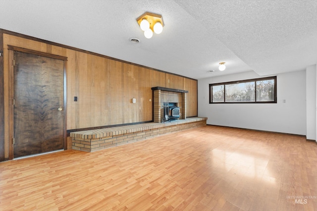 unfurnished living room featuring wooden walls, a textured ceiling, visible vents, and wood finished floors