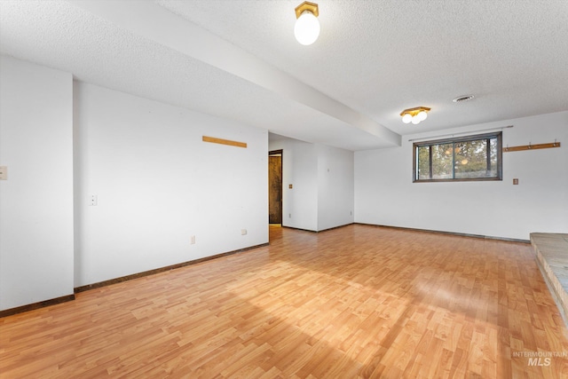 unfurnished room with baseboards, light wood finished floors, and a textured ceiling