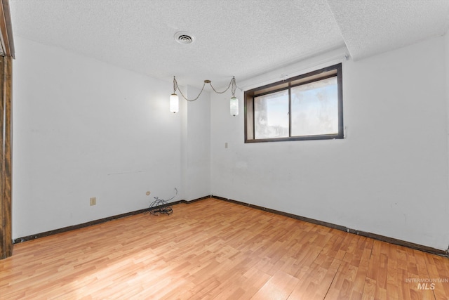 empty room featuring light wood-style flooring, baseboards, visible vents, and a textured ceiling