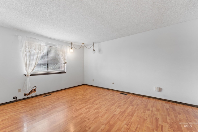 spare room with visible vents, a textured ceiling, baseboards, and wood finished floors