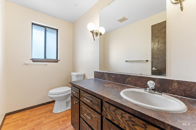 bathroom featuring visible vents, baseboards, toilet, wood finished floors, and vanity