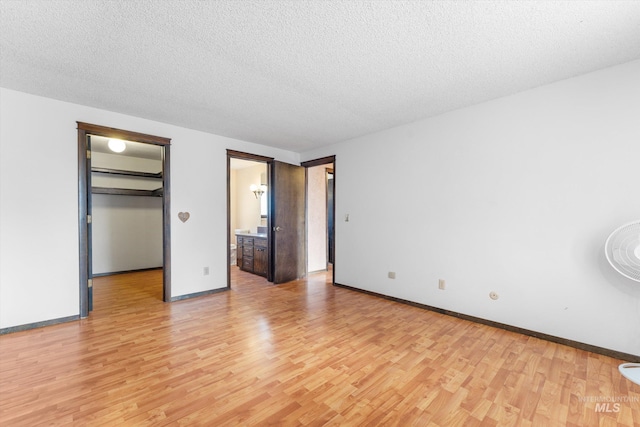 unfurnished bedroom featuring baseboards, a textured ceiling, a spacious closet, and light wood finished floors