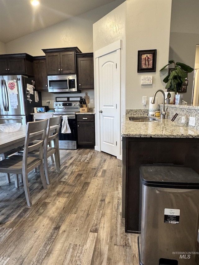 kitchen featuring sink, stainless steel appliances, light stone counters, lofted ceiling, and dark brown cabinets