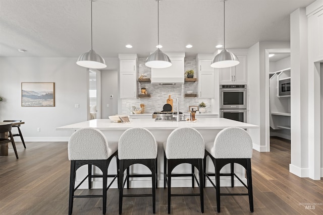 kitchen featuring stainless steel appliances, white cabinets, light countertops, tasteful backsplash, and an island with sink