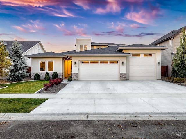 prairie-style house with a garage, concrete driveway, stone siding, a yard, and stucco siding