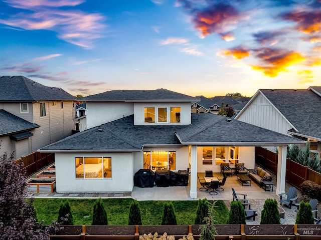 back of house at dusk featuring stucco siding, a shingled roof, a patio area, a fenced backyard, and an outdoor living space