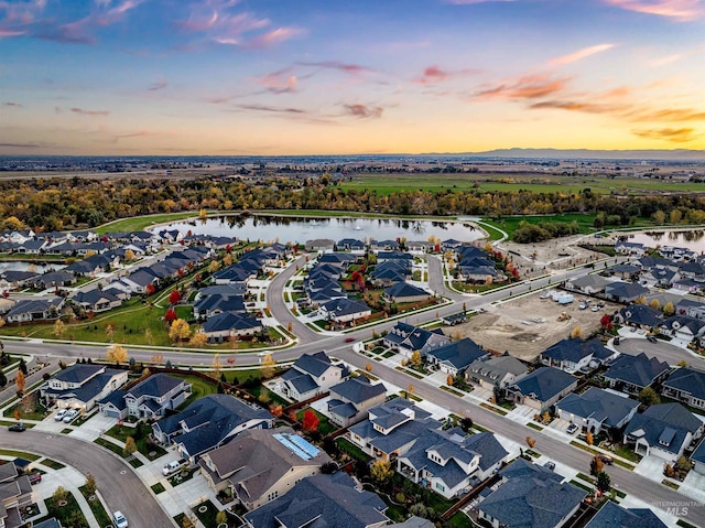 aerial view at dusk with a water view and a residential view