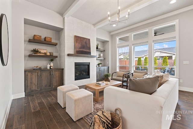 living area featuring built in features, dark wood-type flooring, a tile fireplace, beamed ceiling, and baseboards