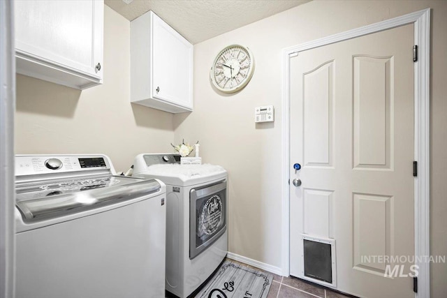 washroom with independent washer and dryer, dark tile patterned floors, a textured ceiling, cabinet space, and baseboards