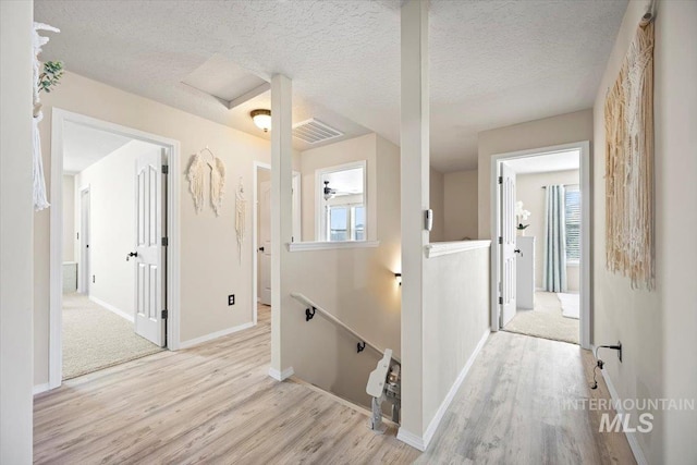 corridor with wood finished floors, visible vents, attic access, a textured ceiling, and an upstairs landing