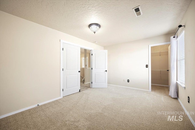 unfurnished bedroom featuring visible vents, a walk in closet, baseboards, light colored carpet, and a textured ceiling