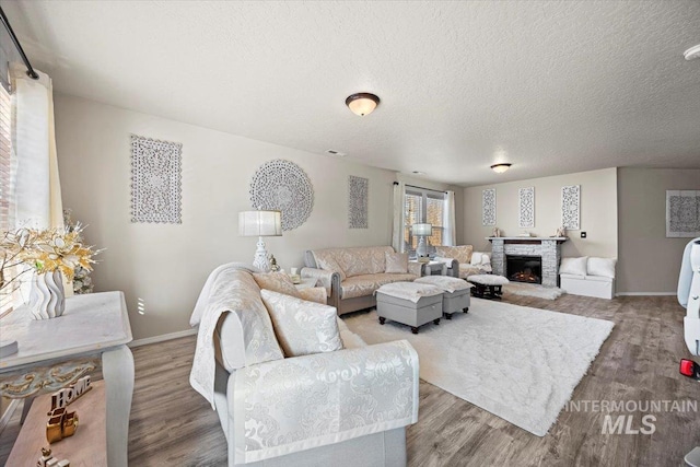 living room with visible vents, baseboards, a stone fireplace, wood finished floors, and a textured ceiling