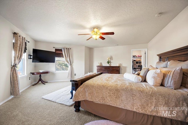 bedroom featuring a walk in closet, a textured ceiling, carpet flooring, baseboards, and ceiling fan