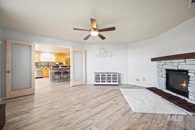 unfurnished living room with visible vents, light wood-style flooring, a textured ceiling, a stone fireplace, and baseboards