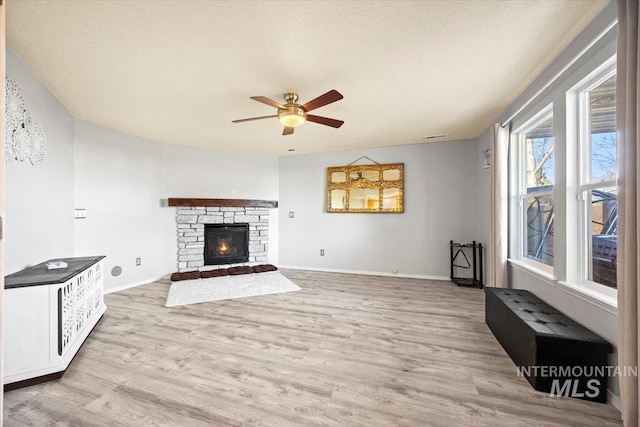 living area with a stone fireplace, a ceiling fan, baseboards, and wood finished floors