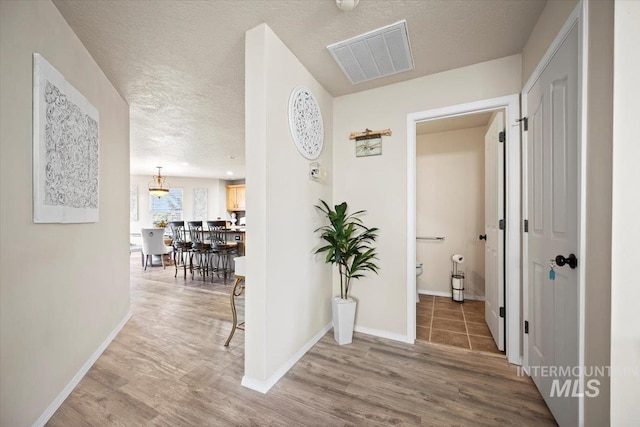 corridor with visible vents, baseboards, a textured ceiling, and wood finished floors