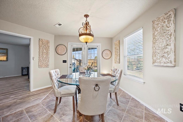 dining space with light tile patterned floors, visible vents, a textured ceiling, and baseboards