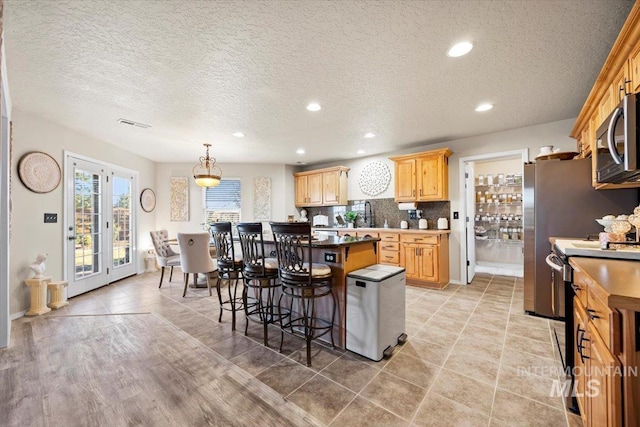 kitchen featuring light brown cabinetry, stainless steel appliances, a kitchen breakfast bar, backsplash, and a center island