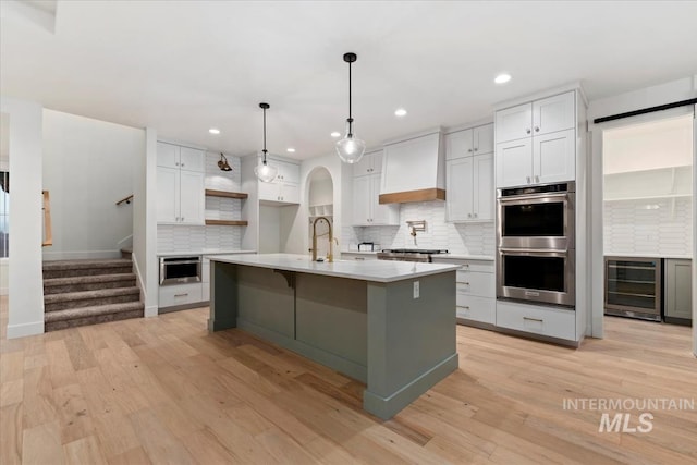 kitchen featuring light countertops, wine cooler, light wood finished floors, stainless steel appliances, and custom range hood