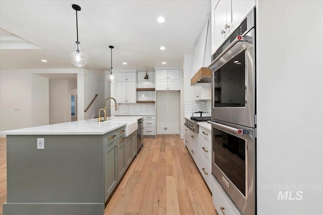 kitchen featuring white cabinetry, light wood-type flooring, a center island with sink, a sink, and appliances with stainless steel finishes