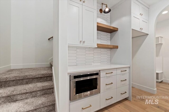 kitchen with light countertops, stainless steel oven, open shelves, white cabinets, and decorative backsplash