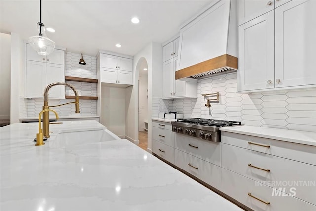 kitchen featuring light stone counters, stainless steel gas cooktop, a sink, premium range hood, and arched walkways