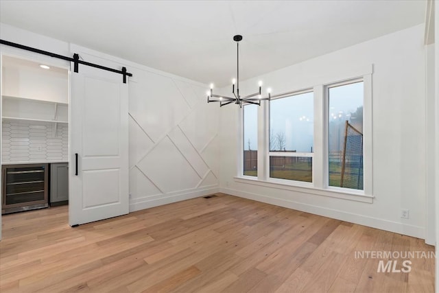 unfurnished dining area with baseboards, a barn door, beverage cooler, light wood-style flooring, and a notable chandelier