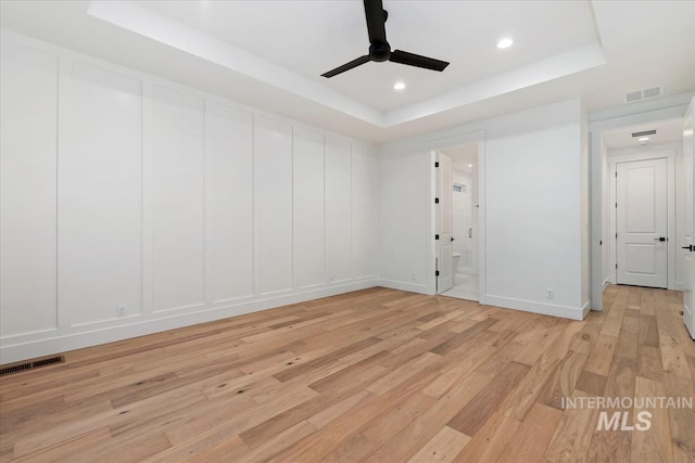 spare room featuring a decorative wall, a tray ceiling, ceiling fan, and visible vents