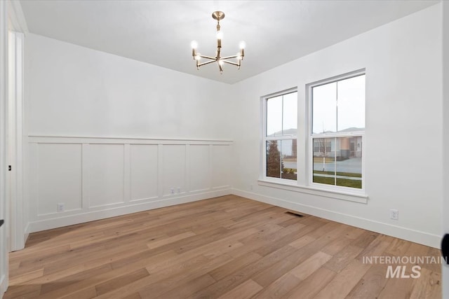 spare room with an inviting chandelier, a decorative wall, light wood-style floors, and visible vents