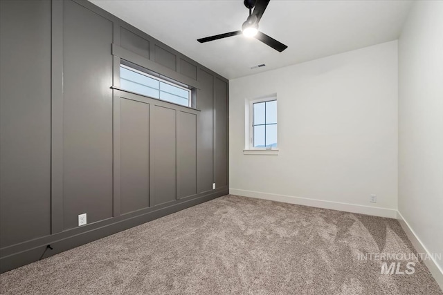 carpeted spare room with baseboards, visible vents, and a ceiling fan