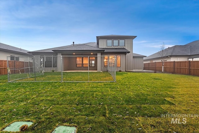 rear view of house with a fenced backyard, board and batten siding, a shingled roof, and a lawn