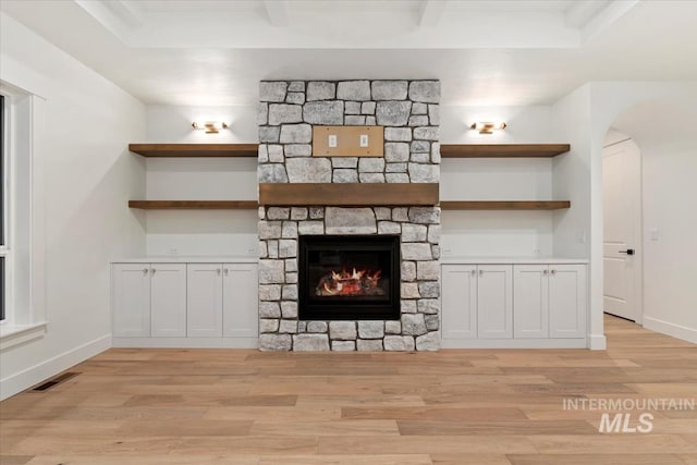 unfurnished living room featuring visible vents, light wood-style flooring, baseboards, a stone fireplace, and arched walkways