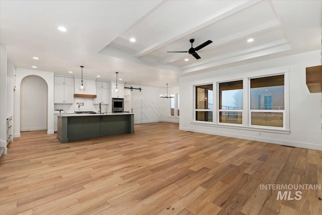kitchen featuring light countertops, tasteful backsplash, light wood-type flooring, ceiling fan with notable chandelier, and arched walkways