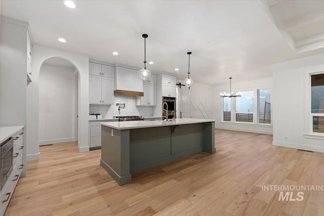 kitchen featuring light wood-style flooring, light countertops, backsplash, and custom exhaust hood