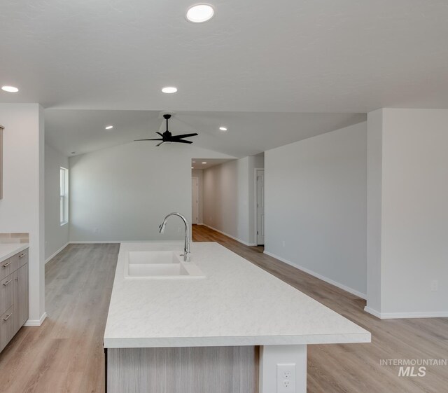 kitchen featuring sink, light hardwood / wood-style flooring, vaulted ceiling, ceiling fan, and an island with sink