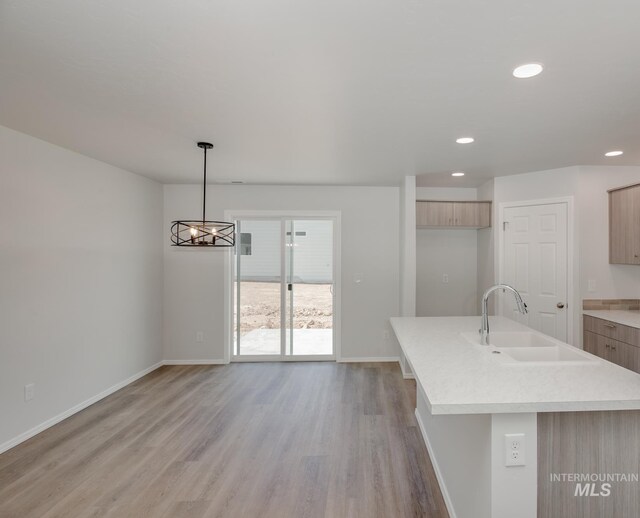 kitchen with sink, pendant lighting, light brown cabinets, a center island with sink, and light hardwood / wood-style flooring