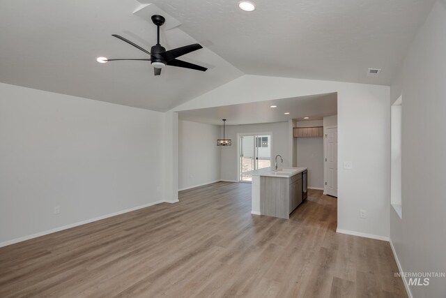 unfurnished living room with ceiling fan with notable chandelier, vaulted ceiling, light hardwood / wood-style flooring, and sink