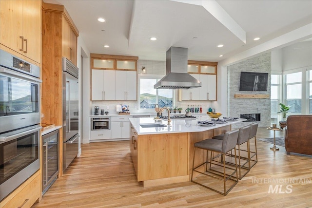 2391 S Trapper Pl, Boise, ID 83716 - kitchen with island range hood, appliances with stainless steel finishes, a sink, wine cooler, and light wood-style flooring
