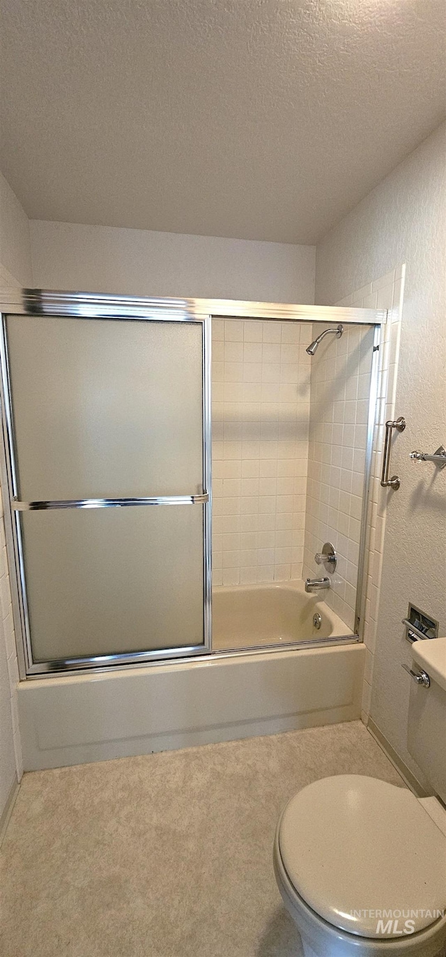 bathroom with a textured ceiling, bath / shower combo with glass door, and toilet