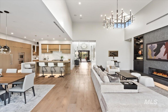 1865 E Lone Shore Ln, Eagle, ID 83616 - living area featuring a towering ceiling, light wood-type flooring, a notable chandelier, a glass covered fireplace, and recessed lighting