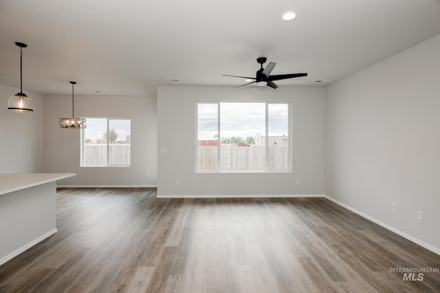 unfurnished living room featuring baseboards, dark wood-style floors, and ceiling fan with notable chandelier