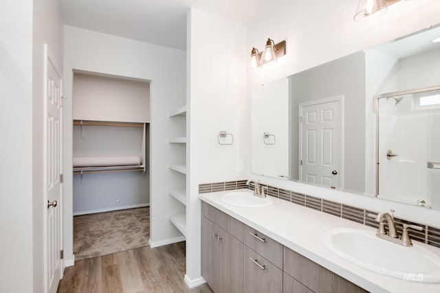 full bathroom featuring a stall shower, double vanity, a sink, and wood finished floors