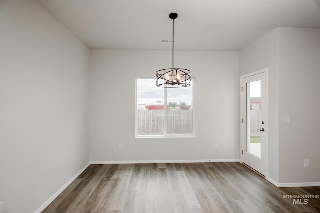 unfurnished dining area featuring baseboards, a notable chandelier, visible vents, and wood finished floors