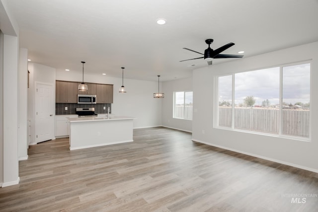 unfurnished living room with light wood finished floors, baseboards, ceiling fan with notable chandelier, and recessed lighting