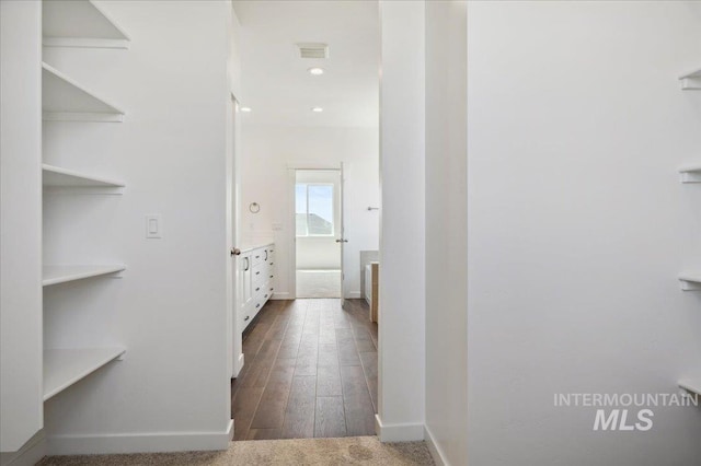 hall featuring visible vents, baseboards, and dark wood-style flooring