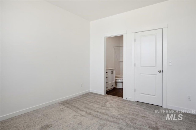 unfurnished bedroom featuring dark carpet, ensuite bath, and baseboards