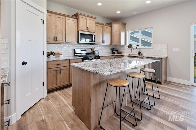 kitchen featuring decorative backsplash, a breakfast bar area, appliances with stainless steel finishes, light wood finished floors, and a sink